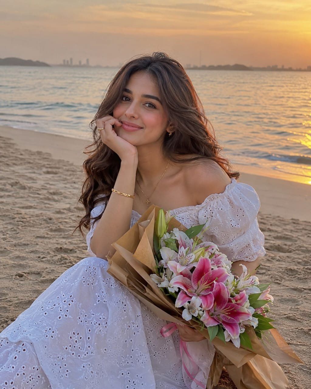 Smiling woman in a white summer dress holding pink and white lilies on a beach at sunset